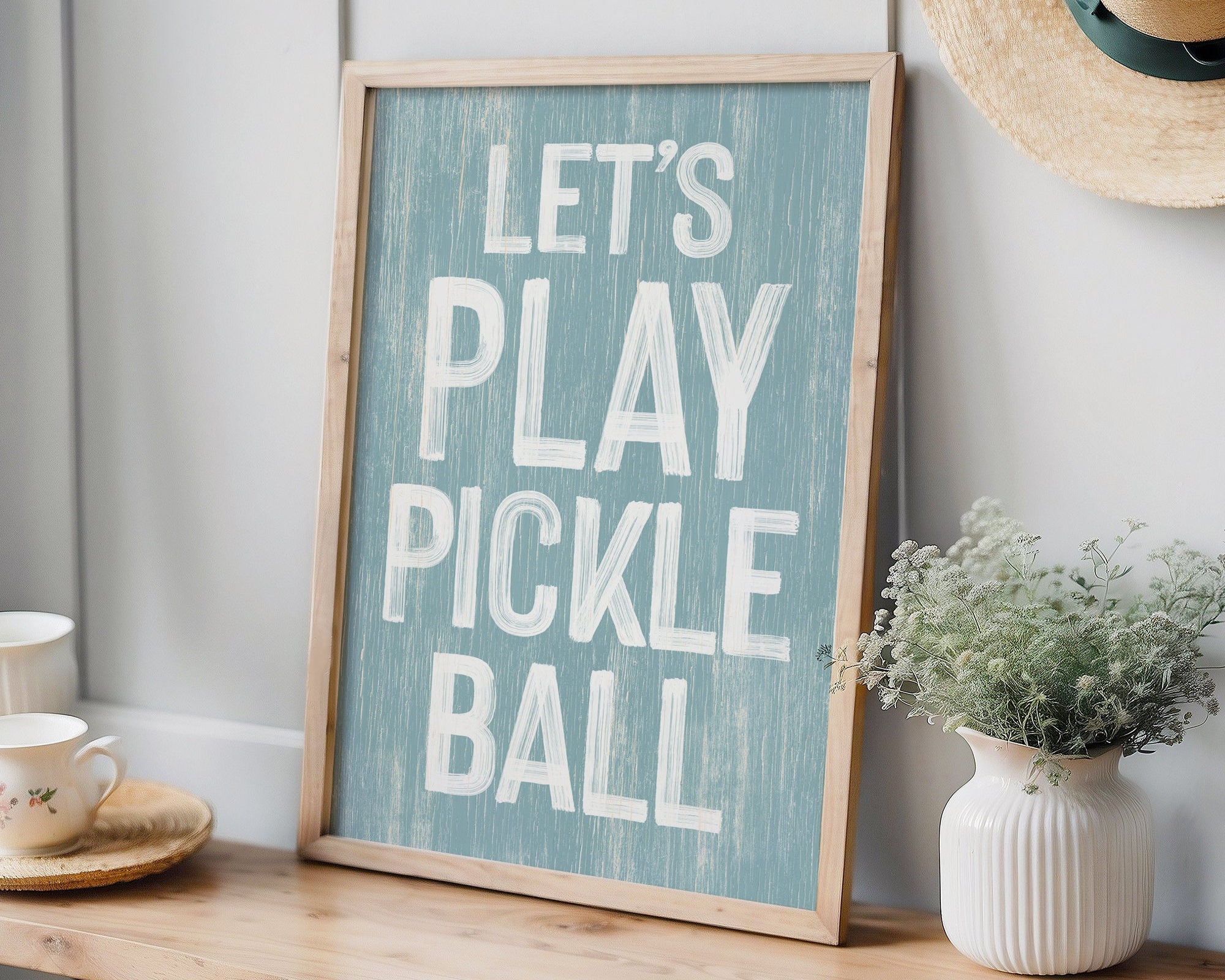 The Let's Play Pickleball Sign, Tide sits on a wooden bench, adding playful wall decor to the scene with a hat, plant, and teacups for modern farmhouse charm.