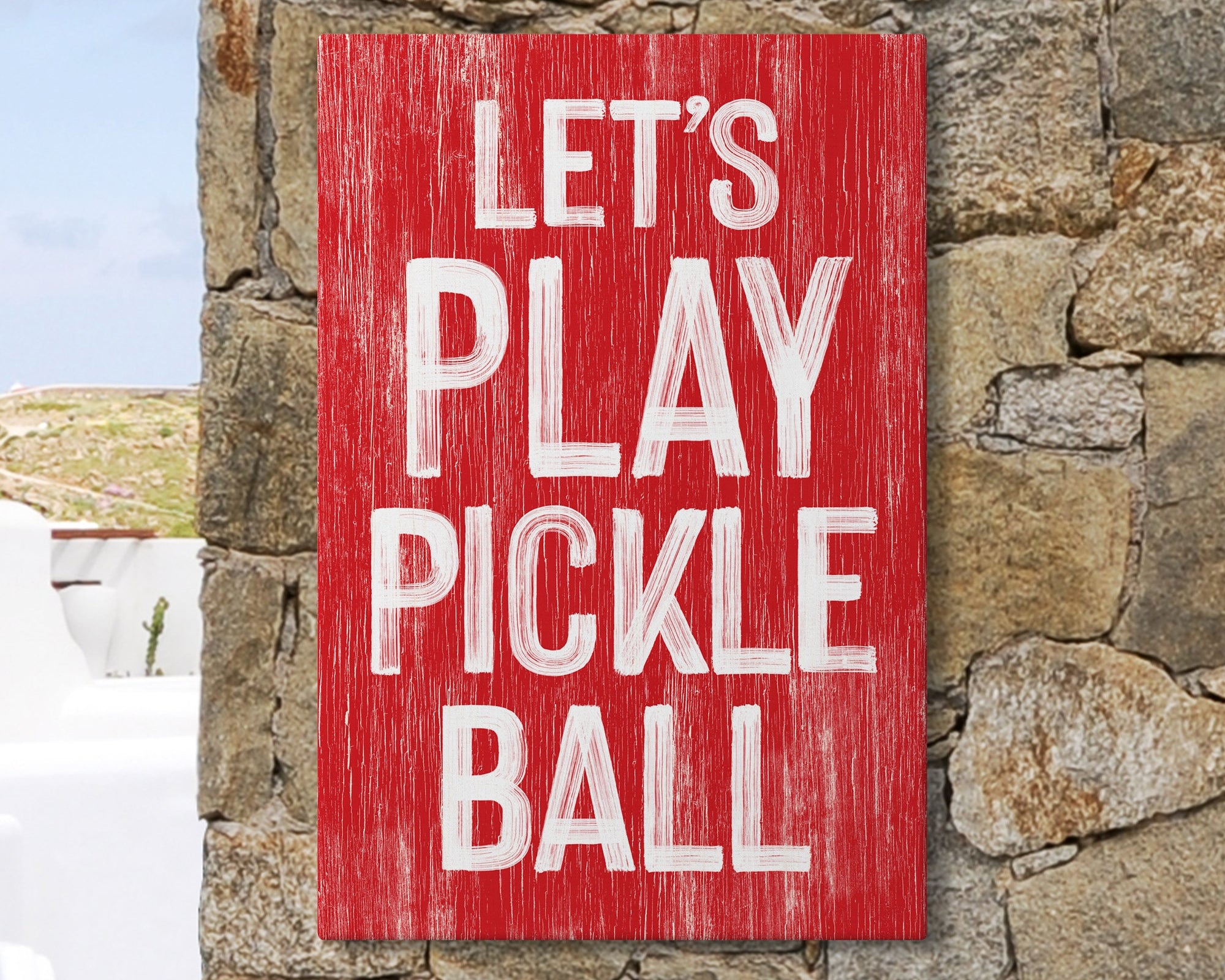 The "Let's Play Pickleball Sign, Real Red" features white text on red wood, shown on a stone wall. This sports-themed decor is perfect for modern farmhouse style.