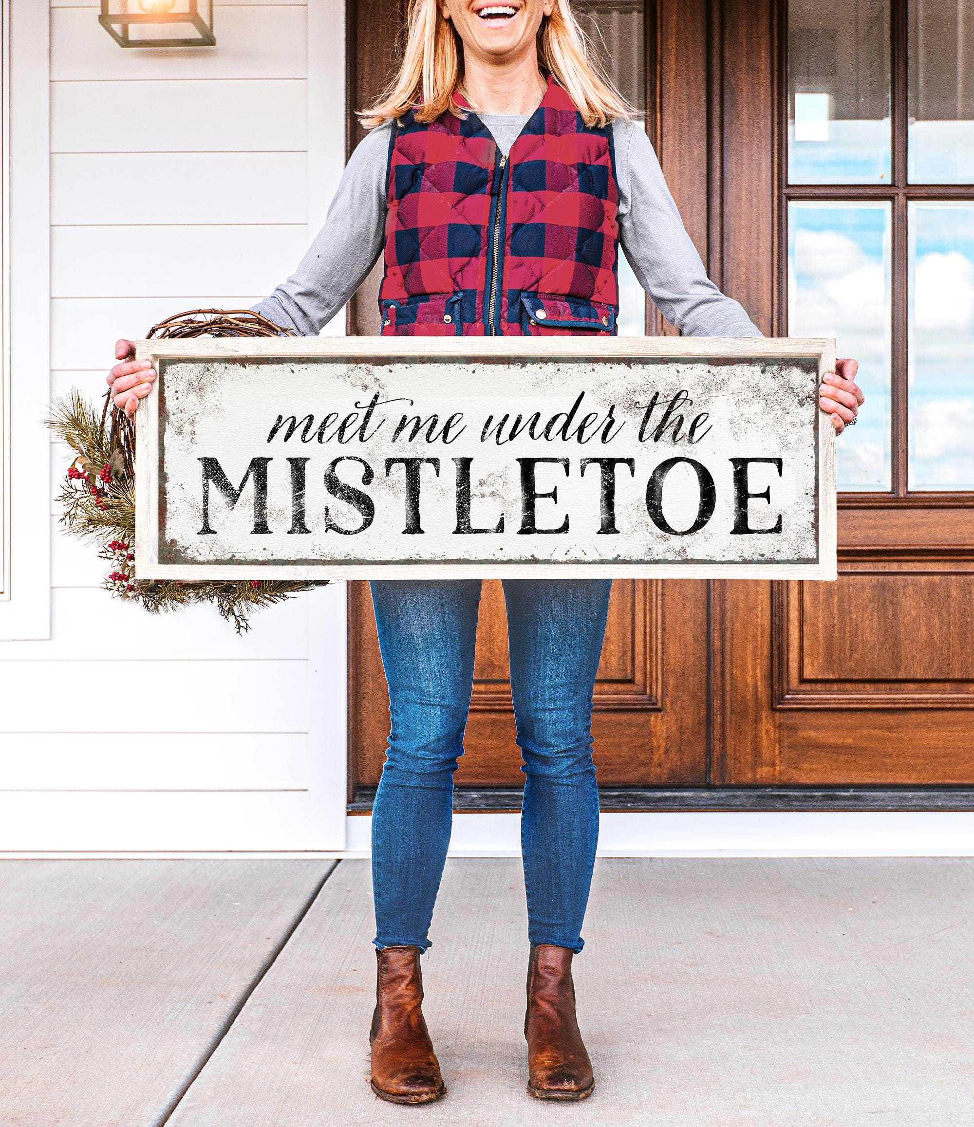 a woman holding a sign that says meet me under the mistletoe