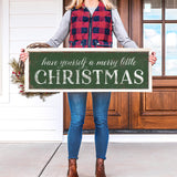 a woman holding a sign that says have yourself a merry little christmas