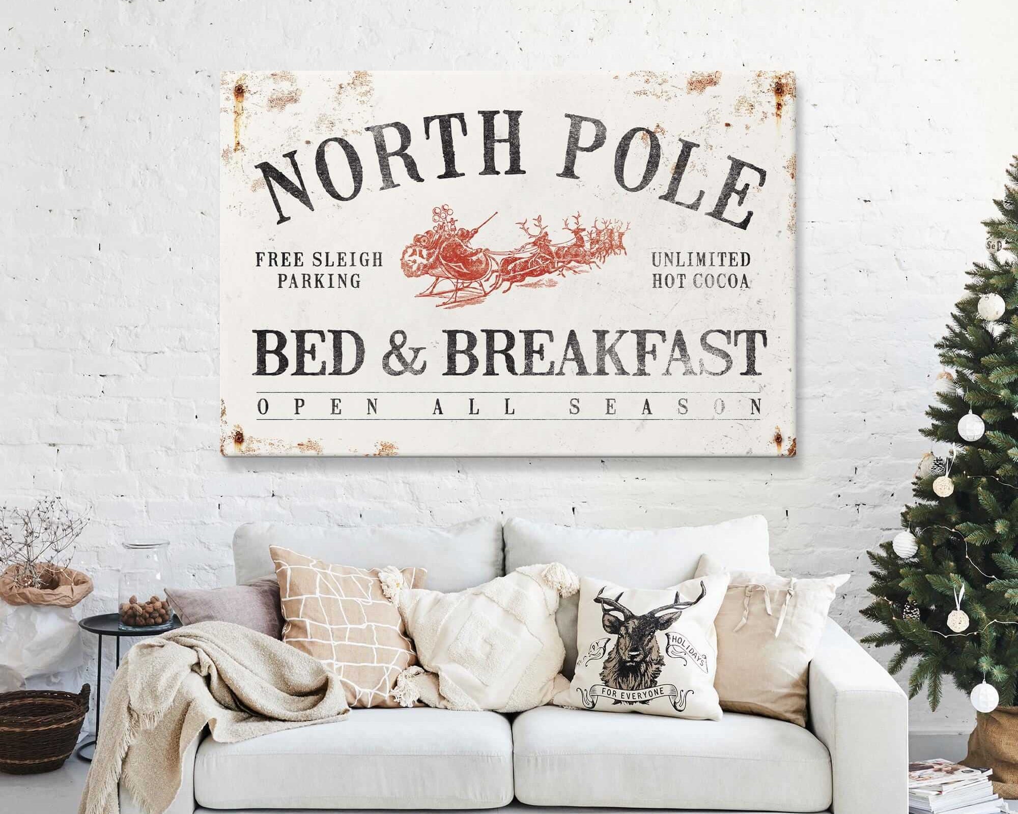 A cozy living room features a sofa, Christmas tree, and the North Pole Bed & Breakfast Sign in white on the wall, bringing festive Christmas wall decor and a modern farmhouse touch.