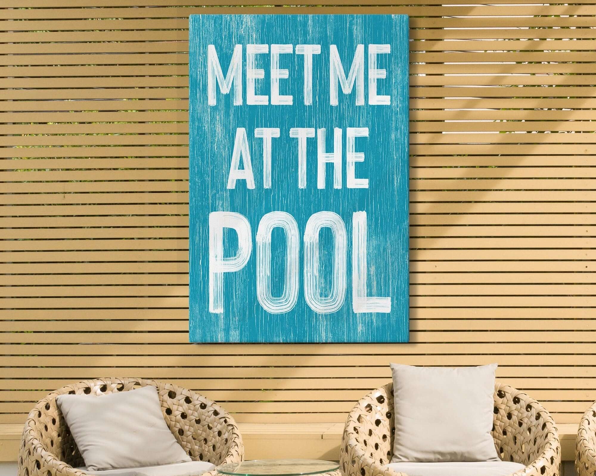 Two wicker chairs and a table sit by a wooden wall with the Meet Me at the Pool Sign, Duck Blue, adding charm to this cozy nook—a perfect touch for vintage home decor fans.