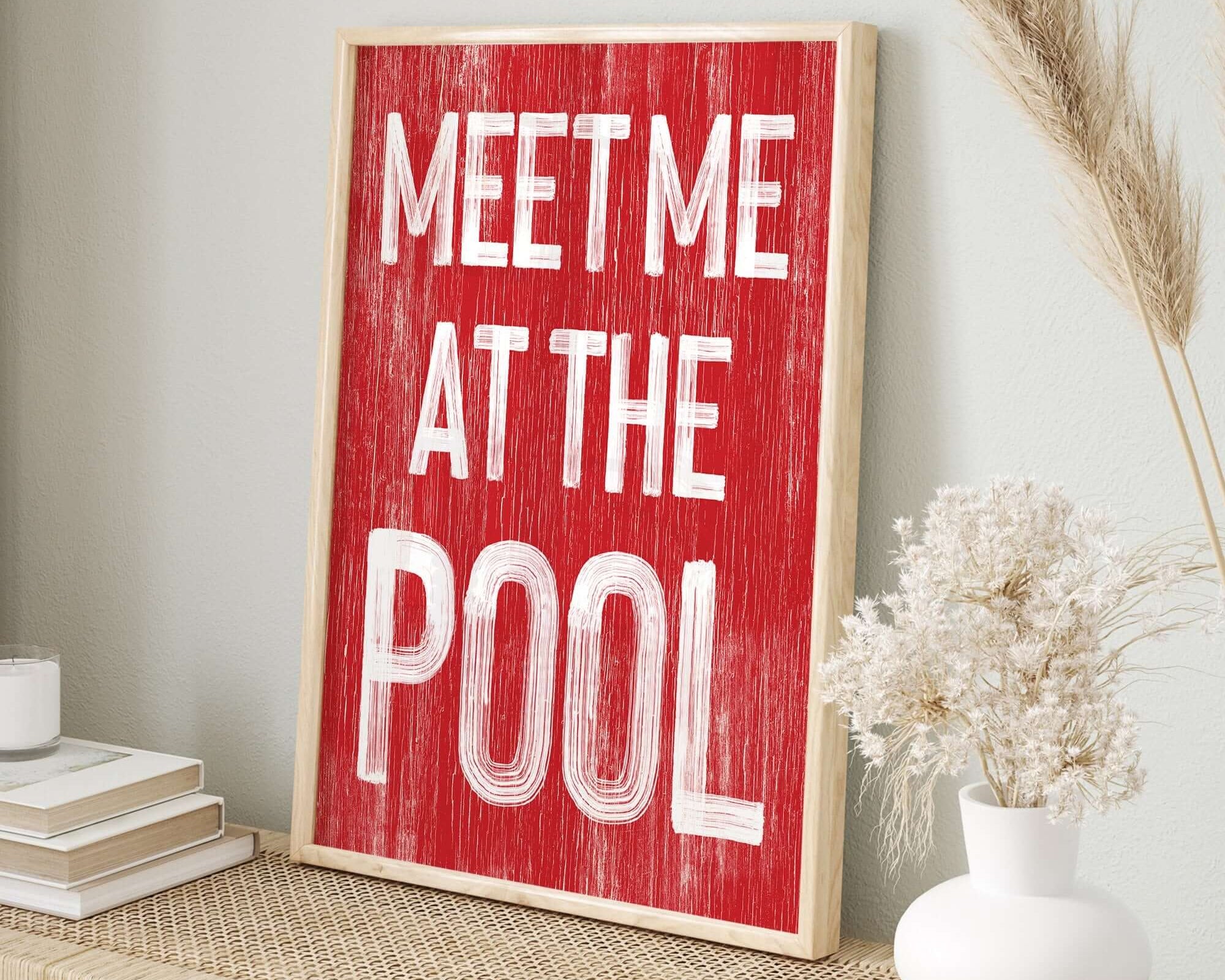 The Meet Me at the Pool Sign, Real Red, features bold white text on a woven tabletop beside books and a vase, bringing vintage charm to your home decor.