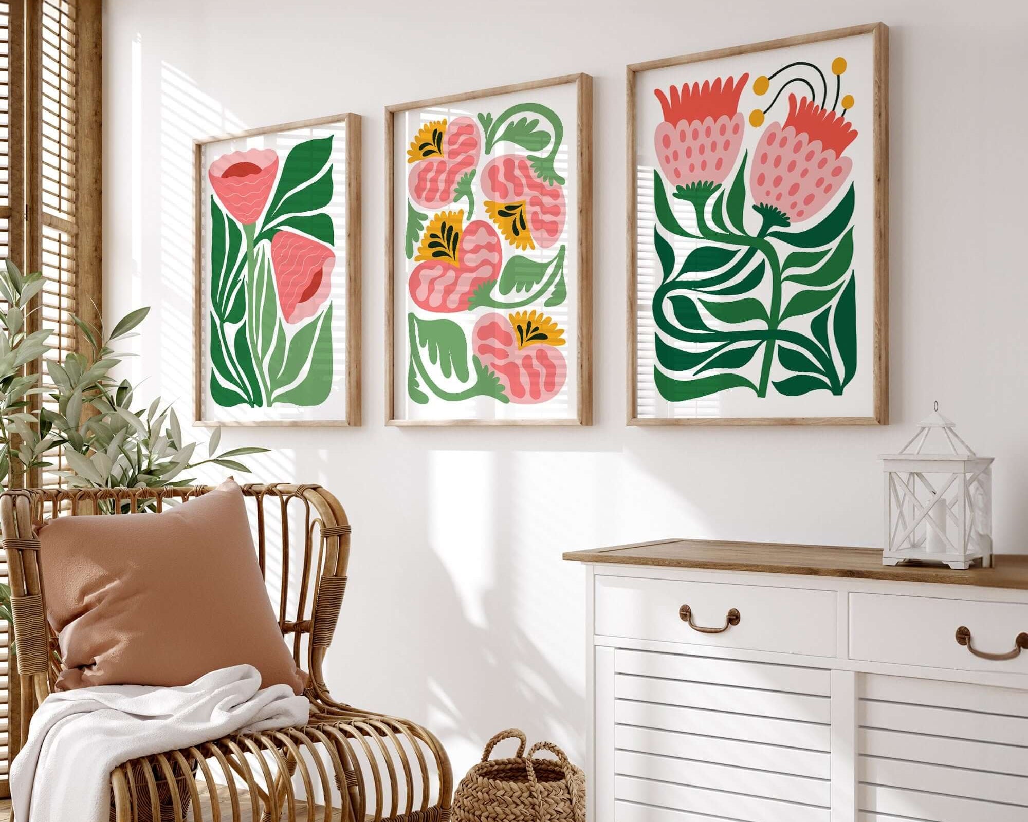 The “Tropical Blocks Triptych | Set of Three Prints | 406” hangs above a rattan chair and white cabinet on a white wall, adding vibrant, tropical flair to the bright room’s decor.