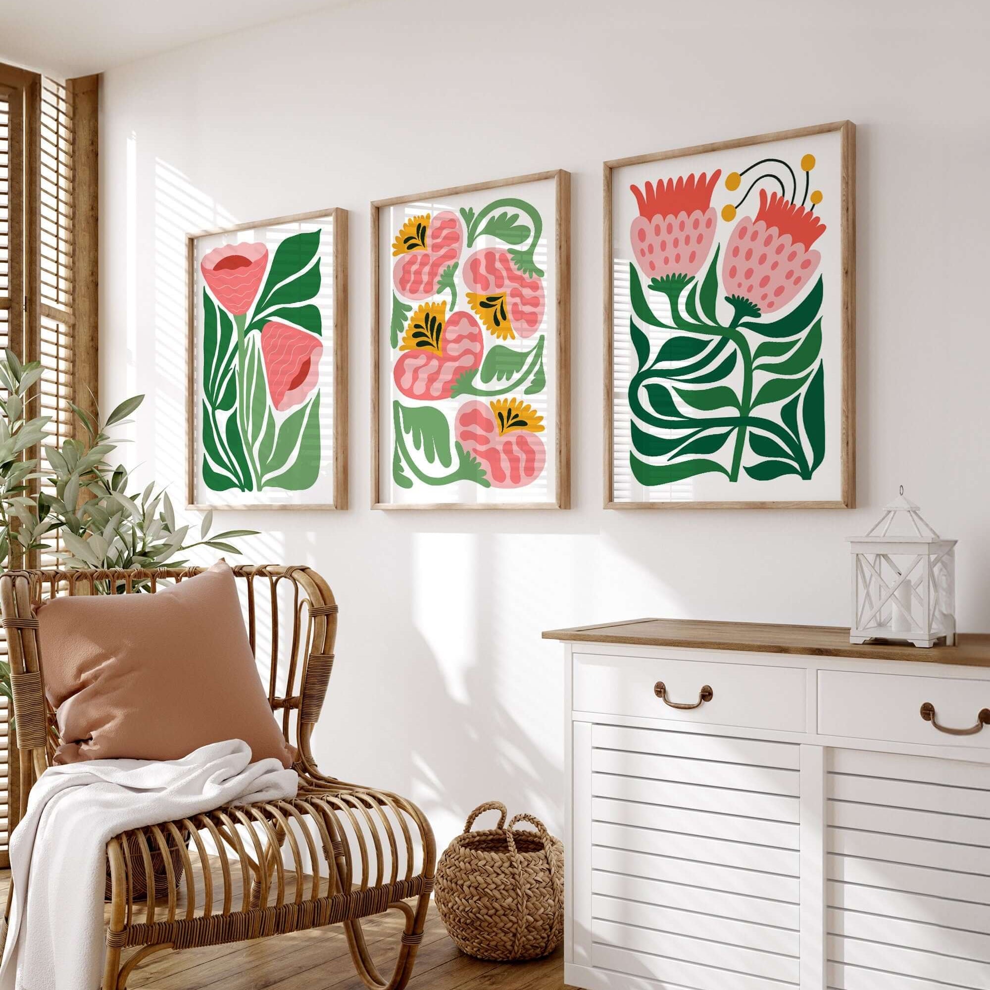 The “Tropical Blocks Triptych | Set of Three Prints | 406” hangs above a rattan chair and white cabinet on a white wall, adding vibrant, tropical flair to the bright room’s decor.