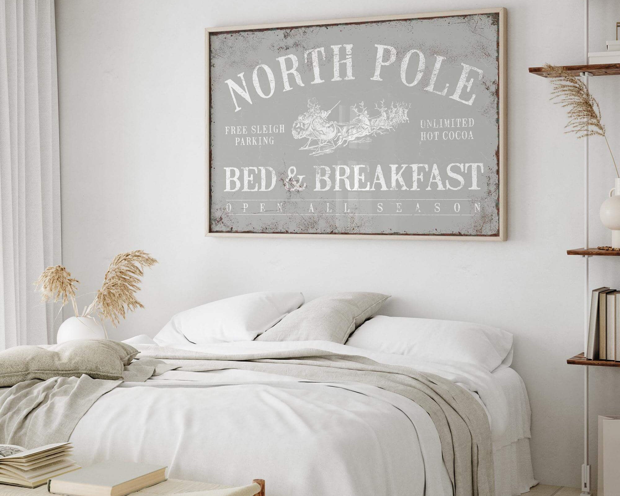 Bright bedroom with white bedding, wood accents, and farmhouse decor, featuring the North Pole Bed & Breakfast Sign in Stone above the bed for a festive touch.