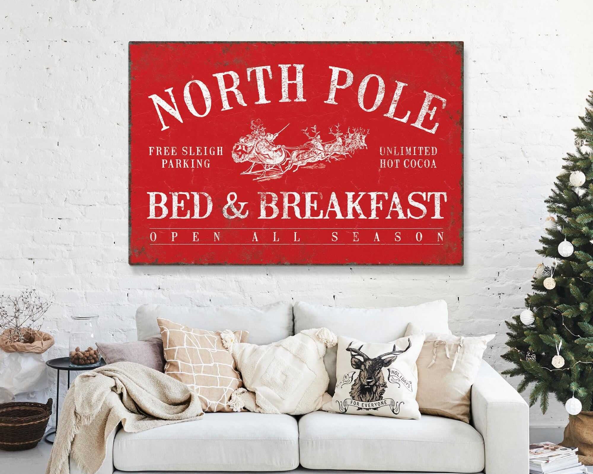 A festive living room with a Christmas tree features the North Pole Bed & Breakfast Sign in Real Red on the wall, adding a charming modern farmhouse accent for the perfect seasonal touch.