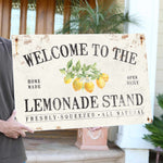 a man holding a welcome to the lemonade stand sign