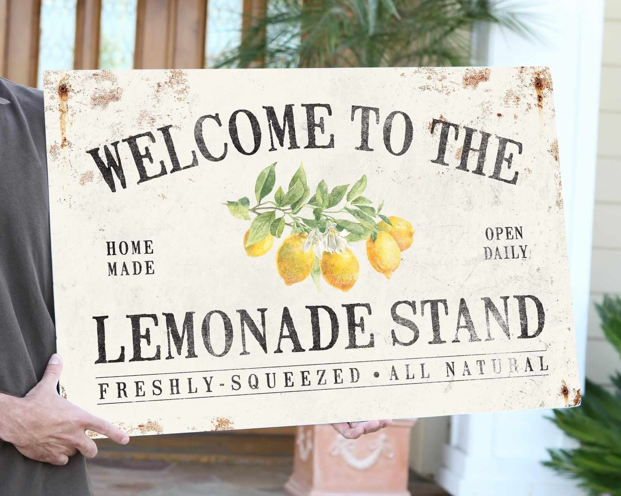 a man holding a welcome to the lemonade stand sign