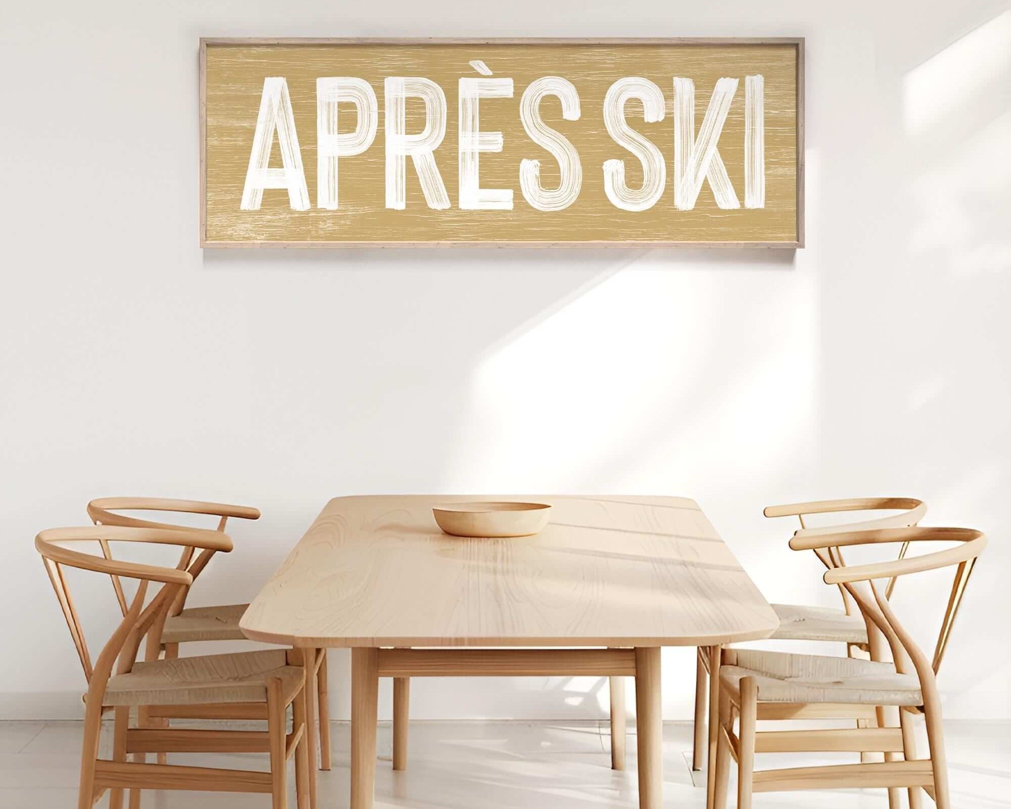 A minimalist dining area features four wooden chairs, a wooden table, and the Apres Ski Sign in Butternut, adding winter charm to this modern farmhouse space.
