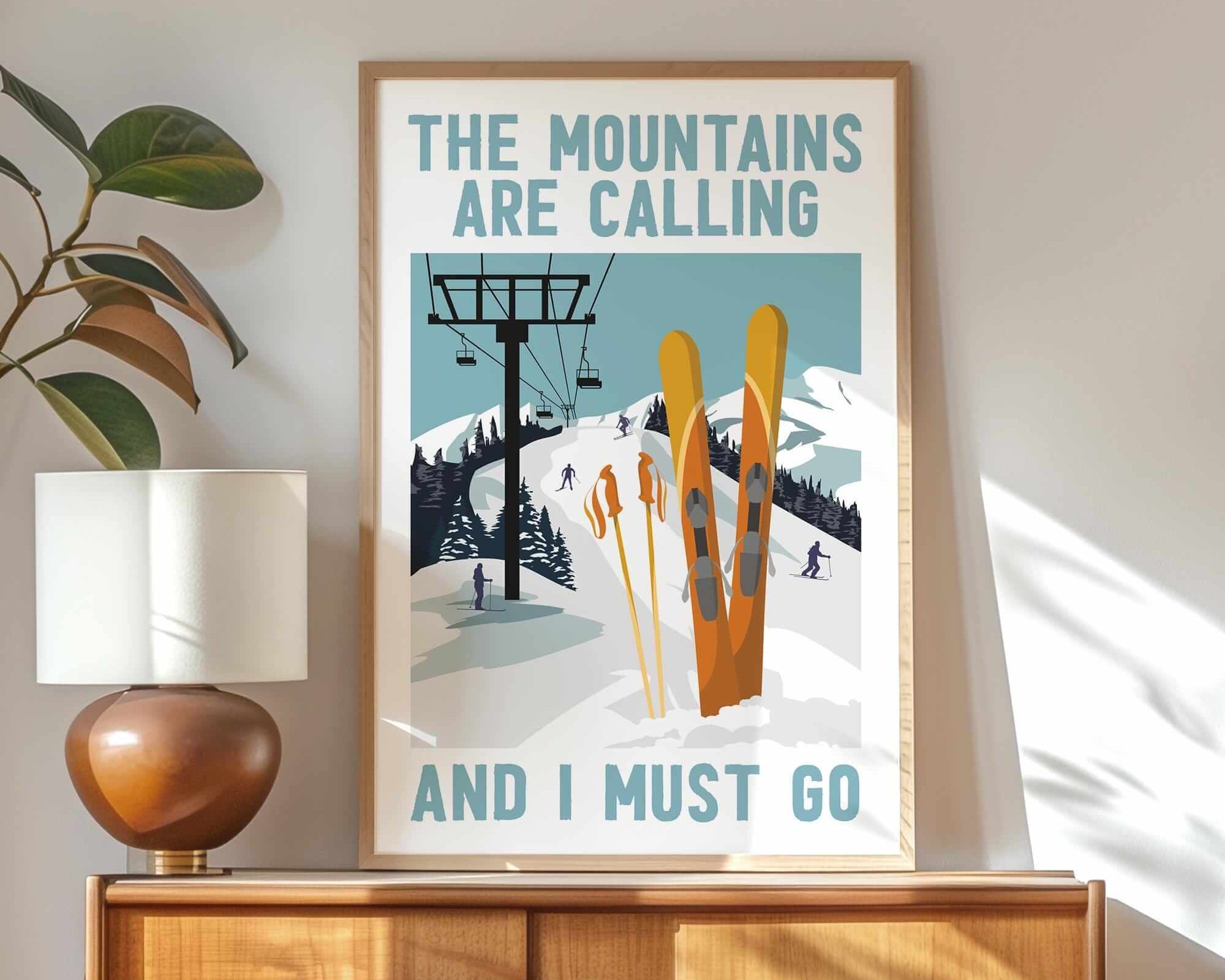 The Mountains Are Calling Retro Ski Poster, Orange, sits framed on a wooden cabinet, adding vintage ski charm and farmhouse appeal with its classic "The mountains are calling and I must go" message.
